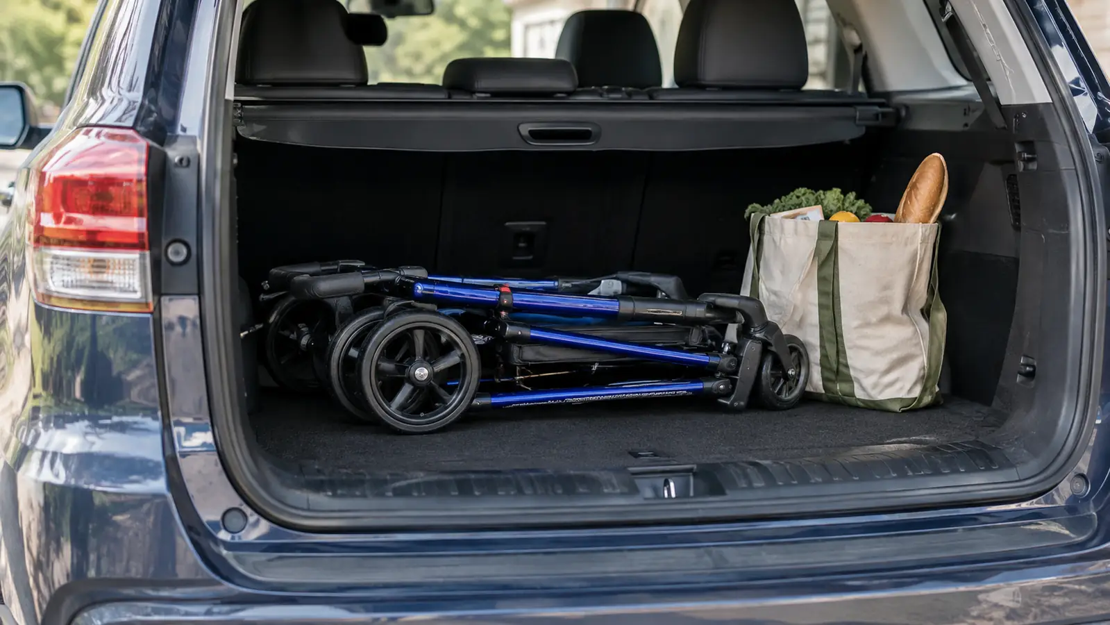 A rollator walker folded flat in the open trunk of a car, with a grocery bag beside it