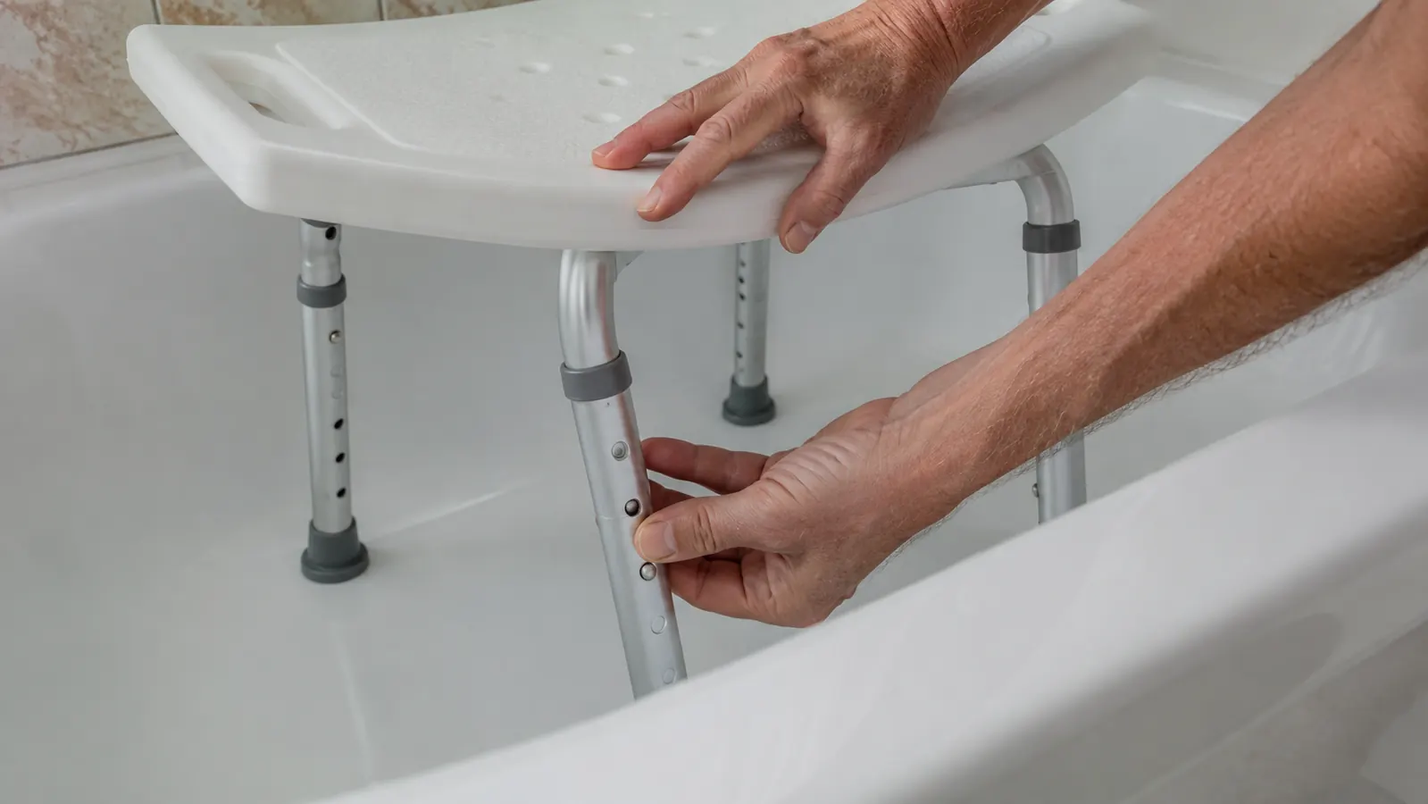 A hand adjusts the leg height on a shower chair set inside a bathtub.