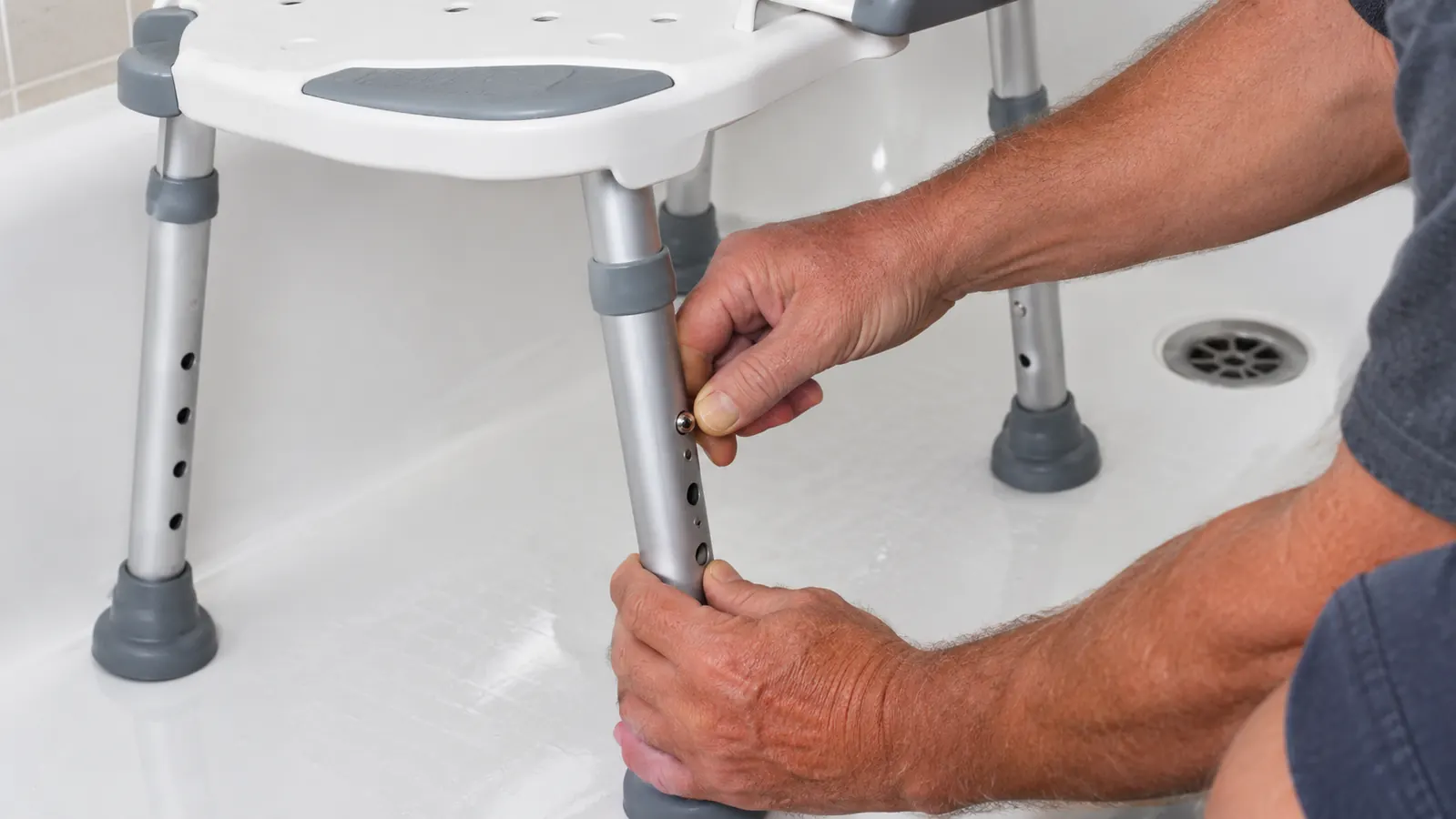A person adjusting the height of a shower chair inside a bathtub, one hand on the seat and one on the leg