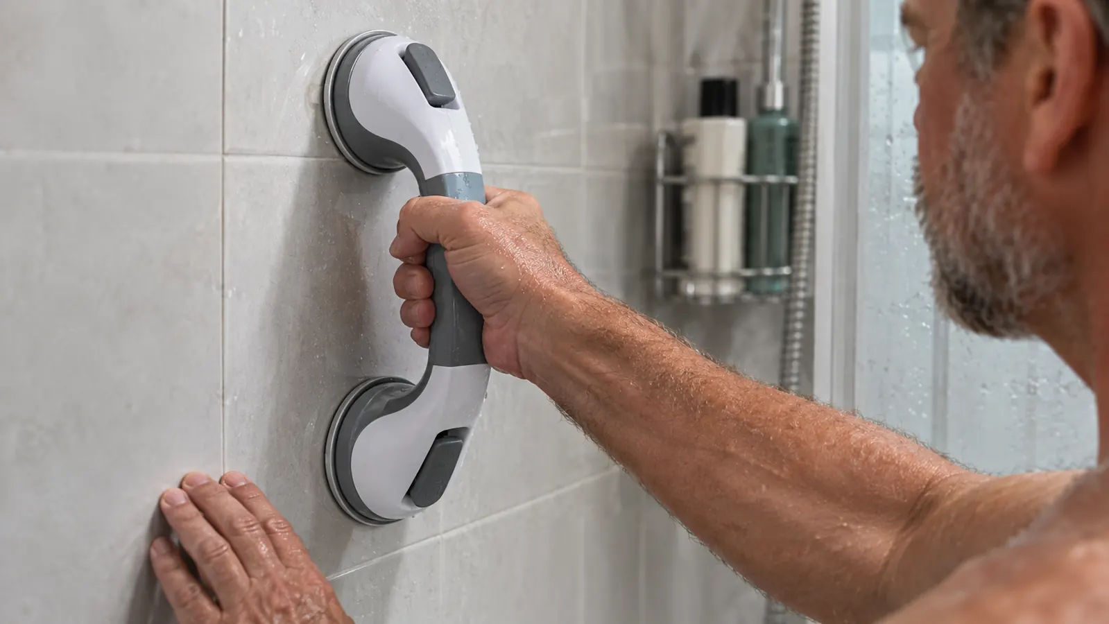 A hand gripping a suction grab bar mounted on smooth tile in a shower